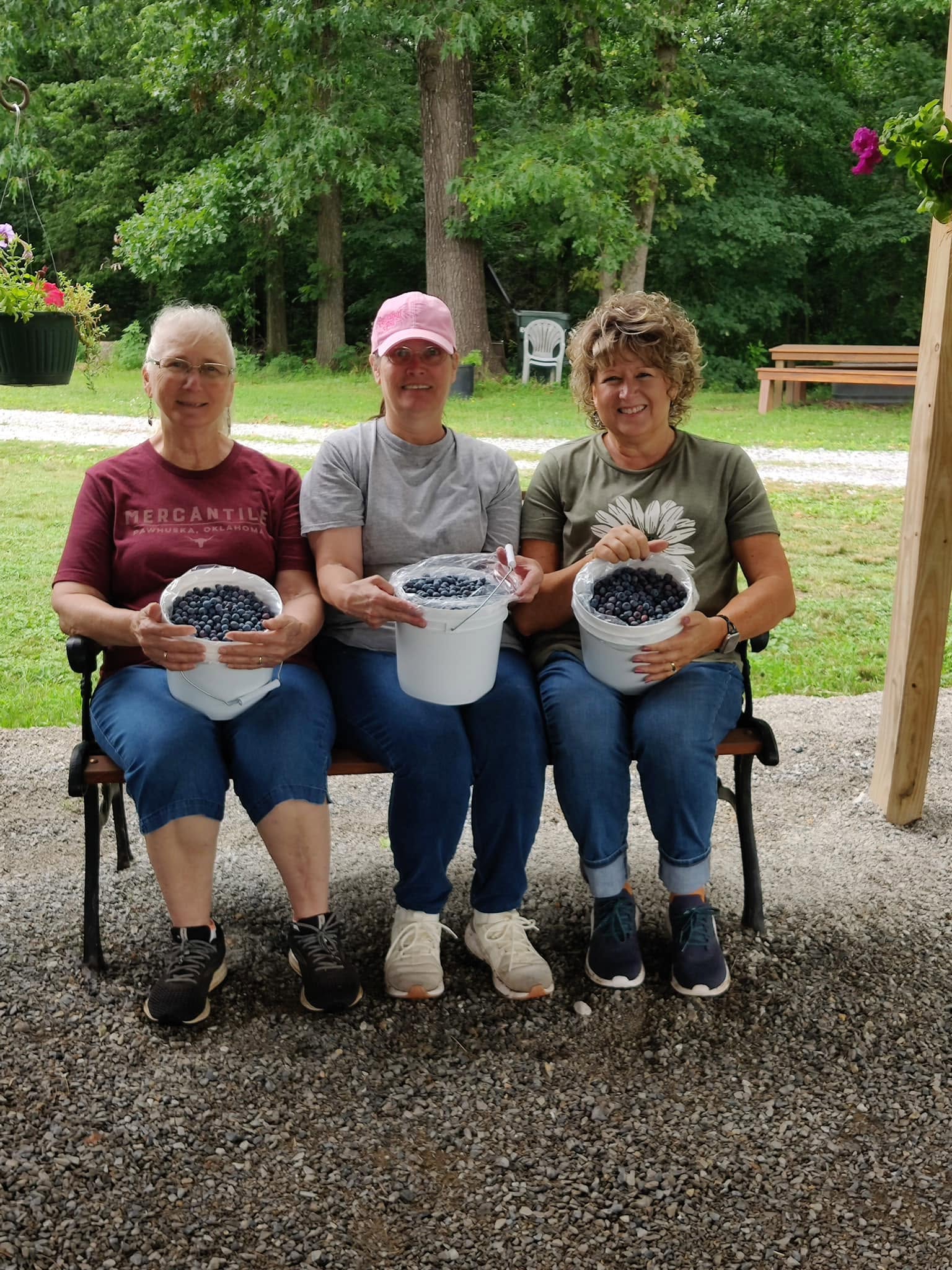 Three women seated outdoors with buckets of freshly picked blueberries